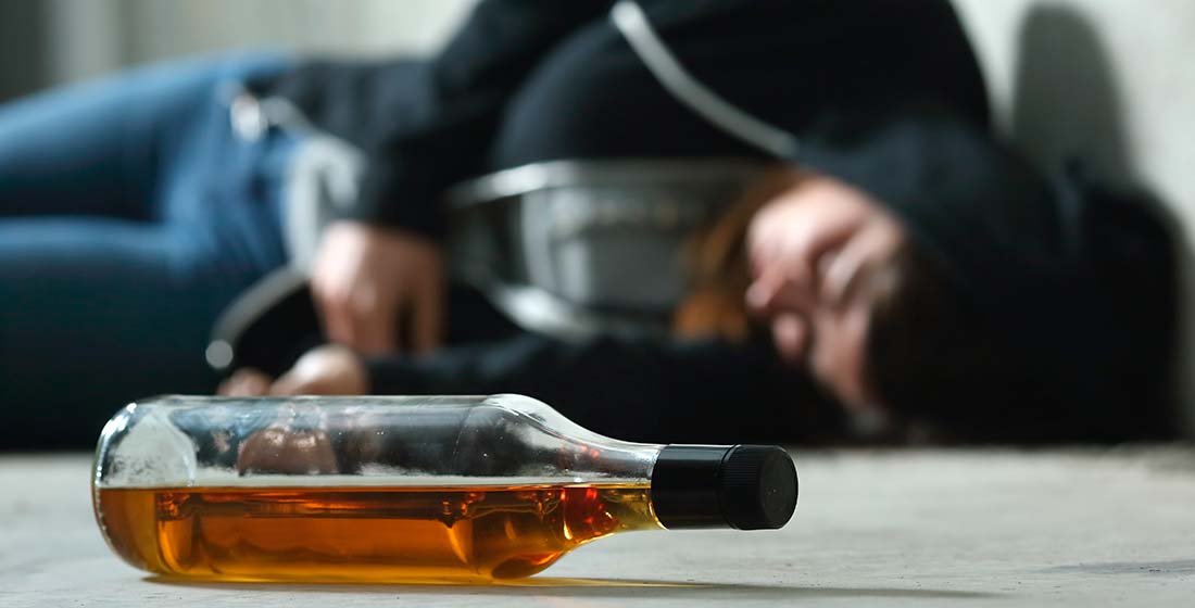 бутылка с алкоголем лежит на полу на фоне спящей на полу девушки