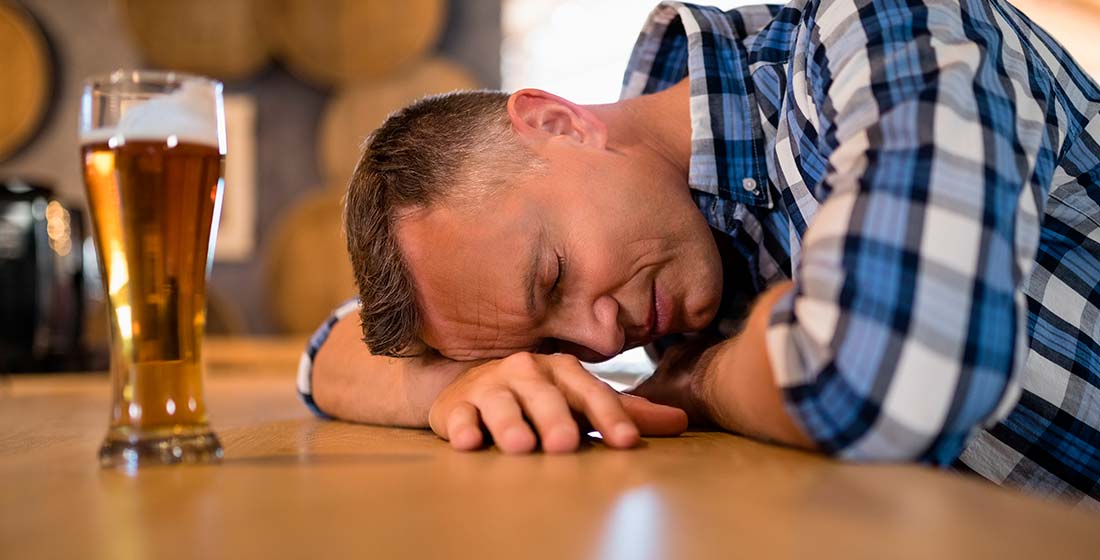 мужчина спит за столом рядом с бокалом пива